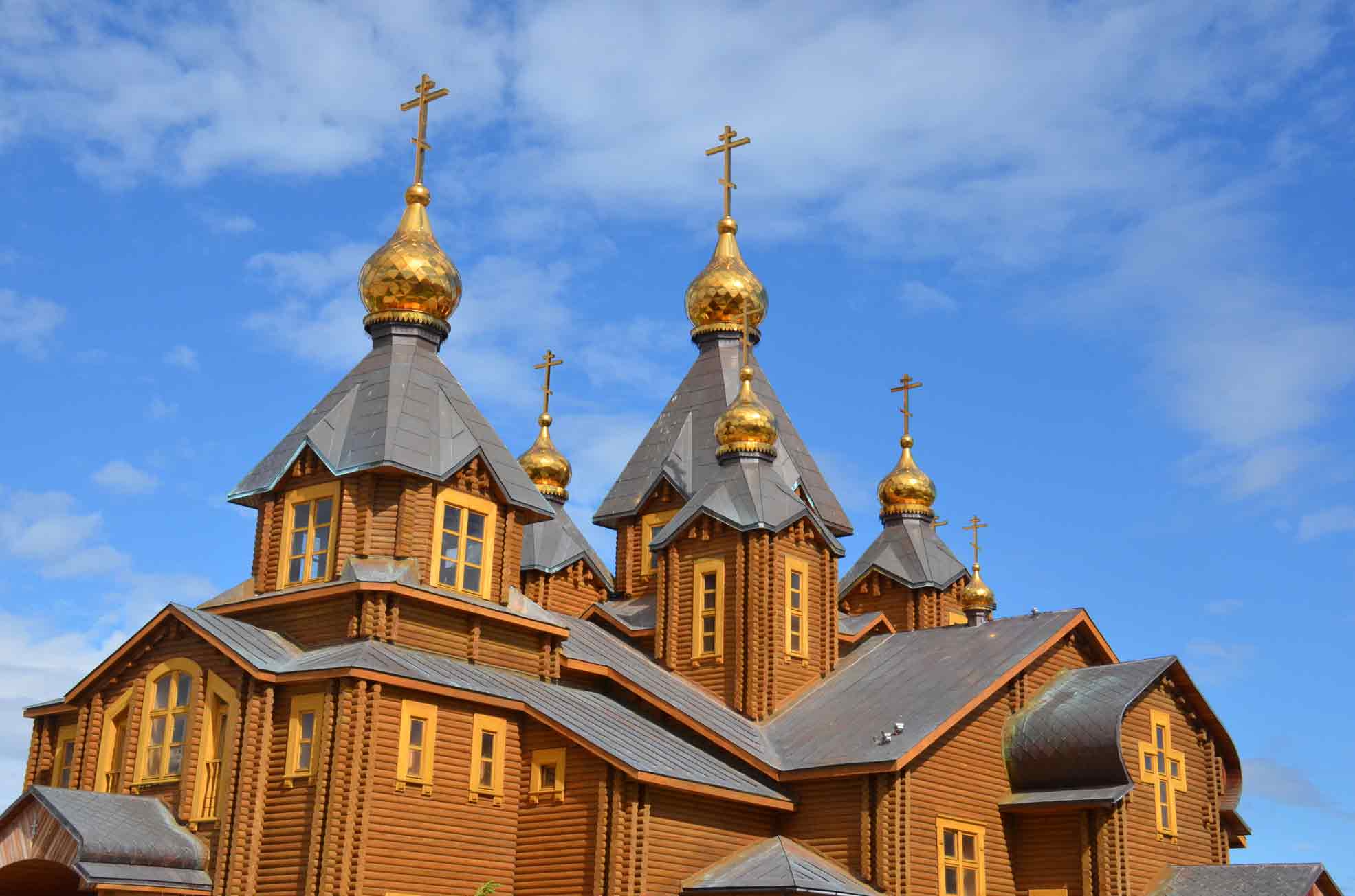 Wooden church with multiple golden onion domes and crosses against a blue sky with clouds