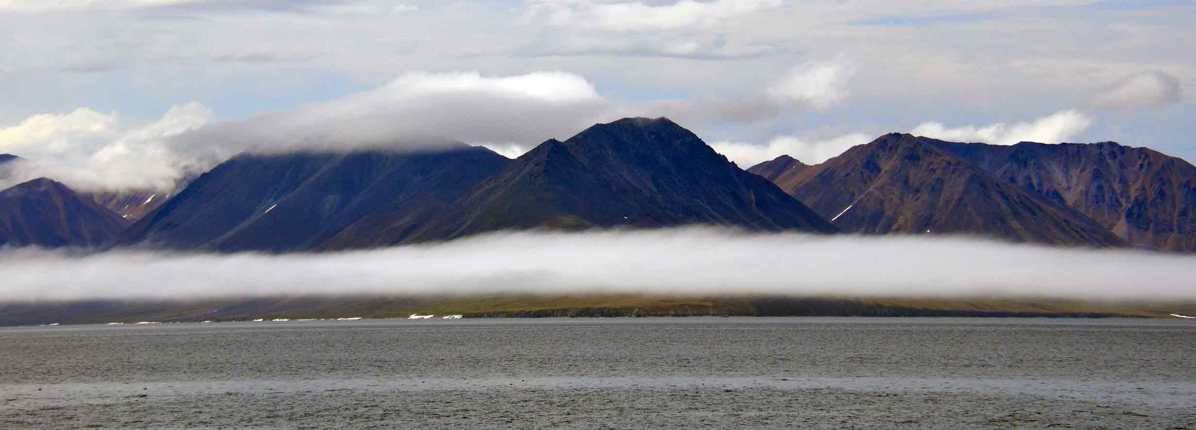 Mountain range partly covered by low clouds and fog above a body of water